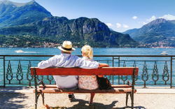Comer See,Dorf Bellagio,Italien. Älterer Paarwochenendenausflug, der Rest auf der Bank durch großartigen See Como in Italien hat. Sonniger Tag Landschaft. Touristen, die Ansicht über populäre Touristenattraktion bewundern.