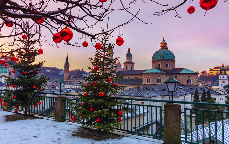 lick auf die historische Stadt Salzburg mit dem berühmten Salzburger Dom im Winter - Weihnachtsbäume mit roten Weihnachtskugeln vor dem Hintergrund des winterlichen Salzburgs - © Natallia - stock.adobe.com
