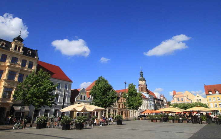 Historischer Marktplatz mit bunten Häusern und Straßencafés bei sonnigem Wetter und blauem Himmel, im Hintergrund ein Kirchturm. - ©holger.l.berlin - stock.adobe.com