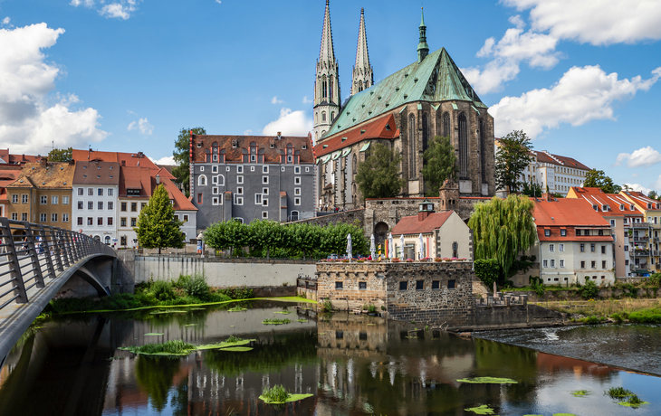 Ein traditionelles deutsches Fachwerkhaus und eine gelbe Kirche in einer malerischen Dorflandschaft vor einem bewaldeten Hügel. - © Isnurnfoto. - stock.adobe.com