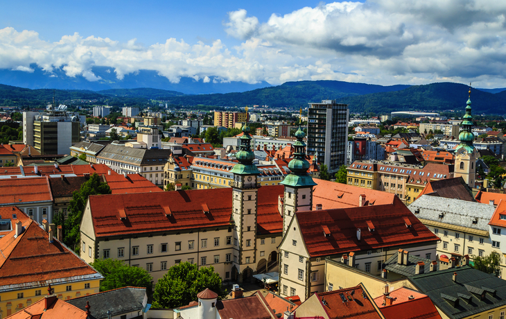 Stadtansicht mit historischen Gebäuden, roten Dächern und Bergen im Hintergrund. - © Silvia Eder - stock.adobe.com