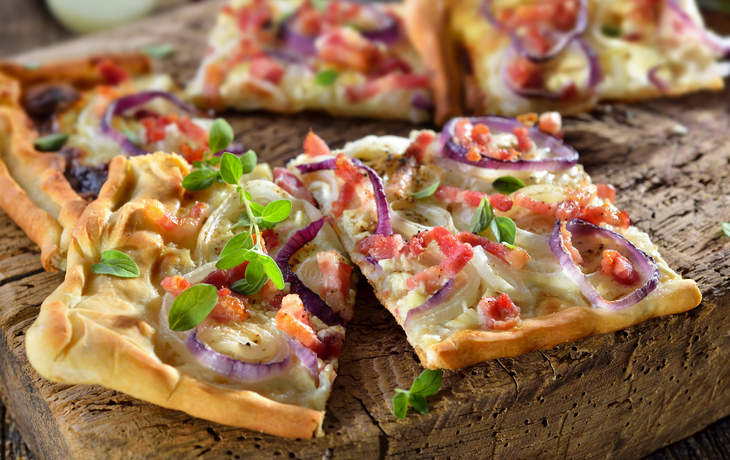 Flammkuchen mit Zwiebeln und Speck auf einem rustikalen Holztisch serviert. - ©kab-vision - stock.adobe.com