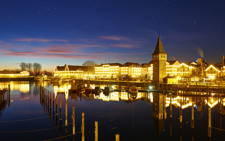 Stadtansicht bei Nacht, beleuchtete Gebäude am Wasser, klarer Himmel. - © Manuel Schönfeld - stock.adobe.com