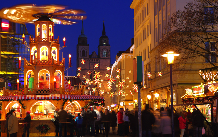 Weihnachtsmarkt mit beleuchteten Ständen und Besuchern in der Dämmerung. - © Horst Schmidt - stock.adobe.com