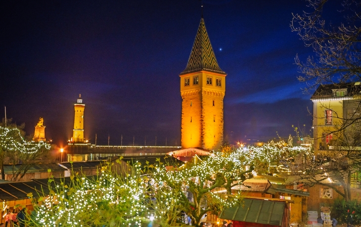 Nachtszene eines beleuchteten Weihnachtsmarktes mit Turm und Baumlichtern. - © hochfeld - stock.adobe.com