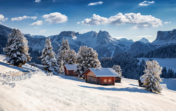 Verschneite Hütten in einer winterlichen Berglandschaft mit Tannenbäumen und strahlend blauem Himmel. - © Andrew Mayovskyy - stock.adobe.com