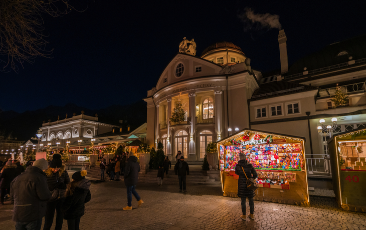Menschen auf einem Weihnachtsmarkt vor einem historischen Gebäude bei Nacht. - ©e55evu - stock.adobe.com