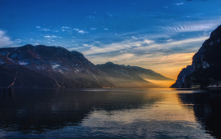 Blick auf den Gardasee im Winter bei Sonnenuntergang, umgeben von Bergen und ruhigem Wasser. - © Barbara - stock.adobe.com
