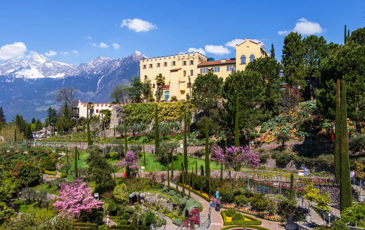 Schloss in malerischer Berglandschaft mit gepflegtem Garten und blühenden Bäumen. - © unununius - stock.adobe.com