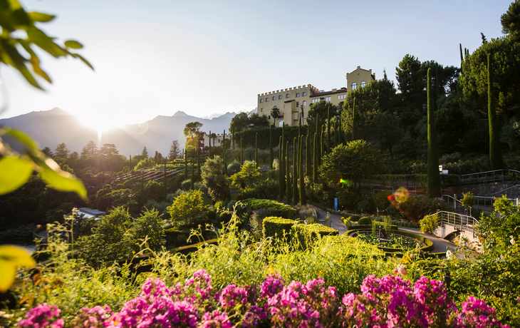 Schloss in malerischer Berglandschaft mit gepflegtem Garten und blühenden Bäumen. - © unununius - stock.adobe.com