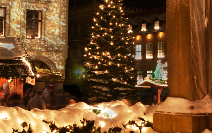 Weihnachtsbaum mit Lichtern in einer verschneiten Stadt bei Nacht - © m. letschert - stock.adobe.com