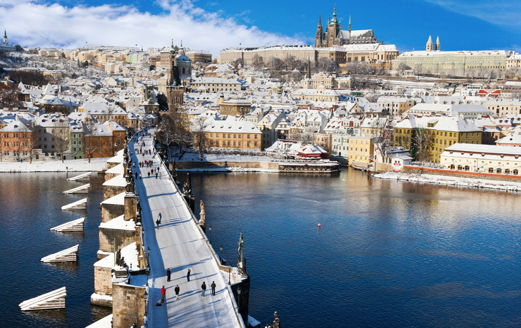 Verschneite Stadtansicht mit Fluss und Brücke, im Hintergrund eine Burg. - © Michaela Jílková - stock.adobe.com