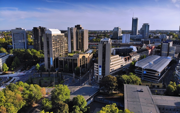 Kirchplatz mit historischem Gebäude und modernen Hochhäusern im Hintergrund - © Sina Ettmer - stock.adobe.com