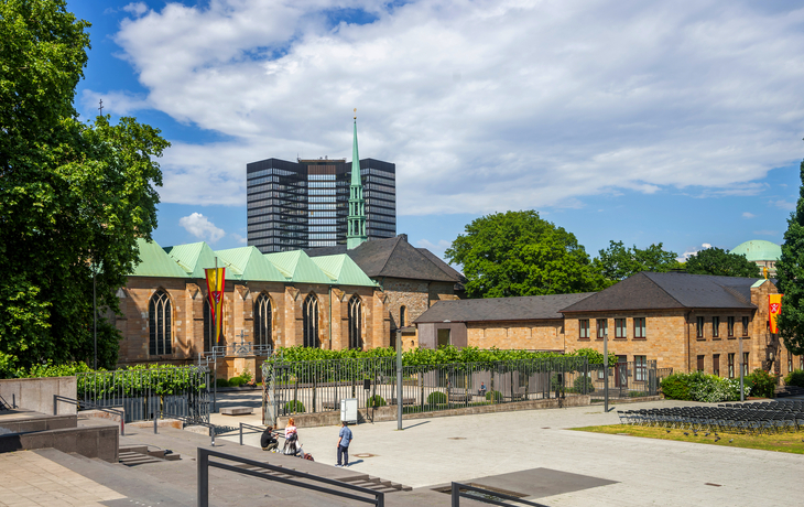Kirchplatz mit historischem Gebäude und modernen Hochhäusern im Hintergrund - © Sina Ettmer - stock.adobe.com