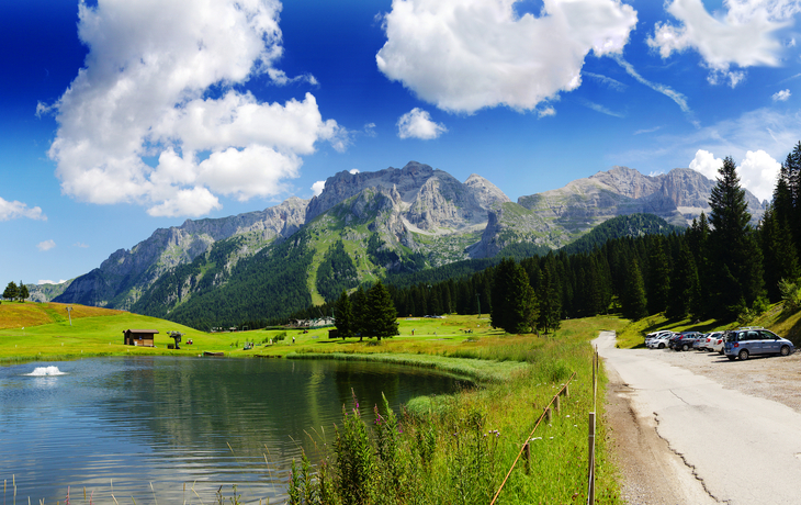 Berglandschaft mit See, Wiese, Bäumen und geparkten Autos unter bewölktem Himmel. - ©pacolinus - stock.adobe.com