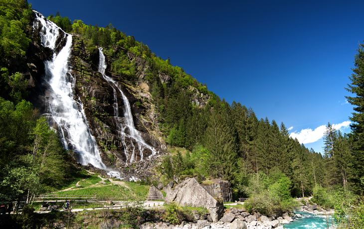 Berglandschaft mit See, Wiese, Bäumen und geparkten Autos unter bewölktem Himmel. - ©pacolinus - stock.adobe.com