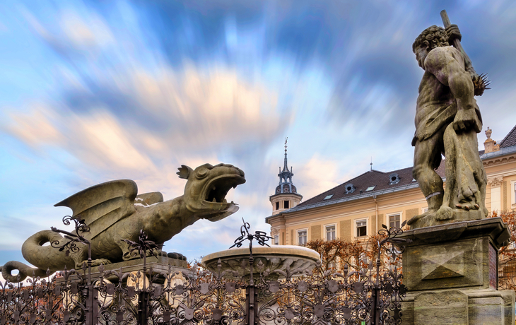 Steinstatue eines Drachen und eines Mannes vor historischer Gebäudekulisse. - © EKH-Pictures - stock.adobe.com