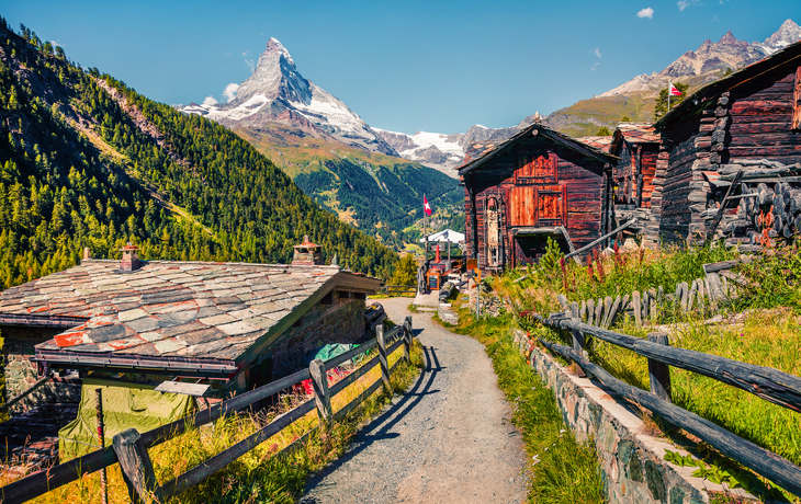 Schafe auf einer Wiese mit einem vorbeifahrenden rot-weißen Zug in einer Berglandschaft - © Gornergrat Bahn
