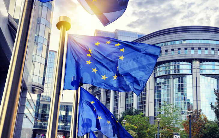 EU-Flaggen wehen vor einem modernen Gebäude in der Sonne. - © Symbiot - stock.adobe.com