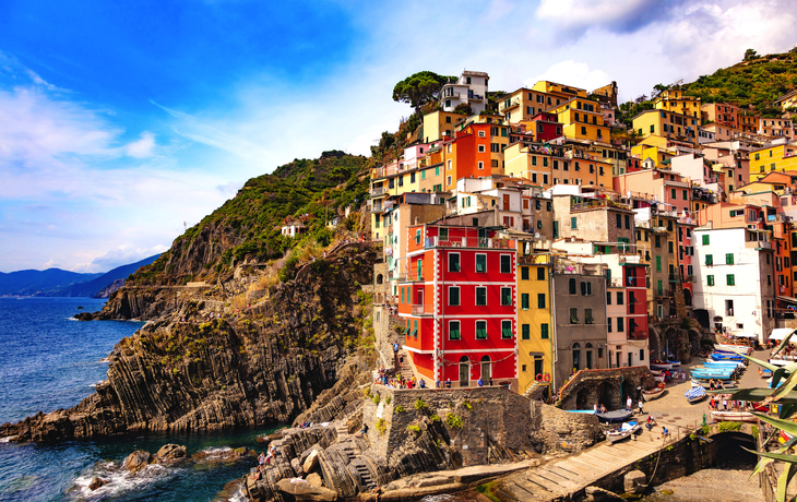 Bunte Häuser von Riomaggiore an der felsigen Küste Italiens unter blauem Himmel. - ©Warpedgalerie - stock.adobe.com
