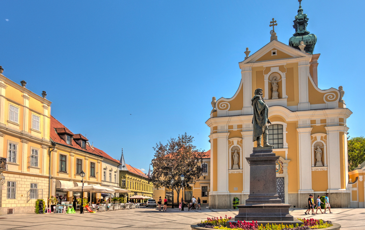Platz mit Statue, barocker Kirche und Gebäuden unter blauem Himmel. - © mehdi33300 - stock.adobe.com