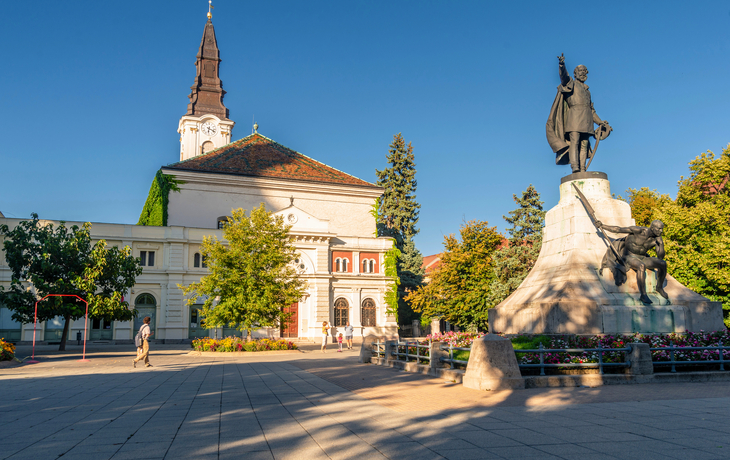 Platz mit Statue, barocker Kirche und Gebäuden unter blauem Himmel. - © mehdi33300 - stock.adobe.com