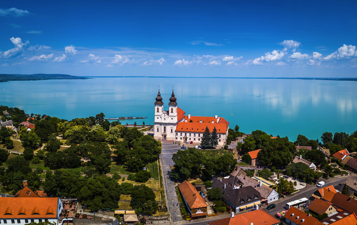 Luftaufnahme einer Kirche am Balaton-See mit umliegendem Dorf und blauem Himmel. - ©zgphotography - stock.adobe.com