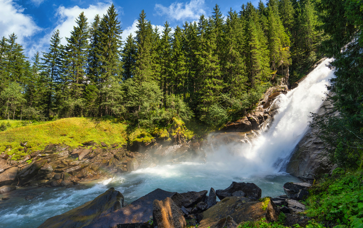 Wasserfall in einem Waldgebiet unter blauem Himmel und Sonne. - © Comofoto - stock.adobe.com