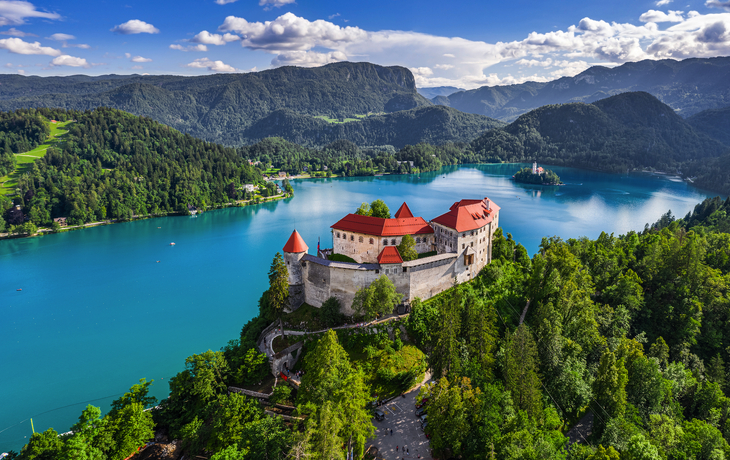 Insel mit Kirche in einem türkisfarbenen See, umgeben von bewaldeten Bergen. - © oneblink1 - stock.adobe.com