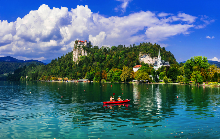Insel mit Kirche in einem türkisfarbenen See, umgeben von bewaldeten Bergen. - © oneblink1 - stock.adobe.com