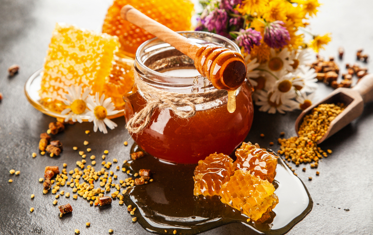 Ein Glas Honig mit Holzlöffel und Bienenwabe auf einem Tisch. - © George Dolgikh - stock.adobe.com